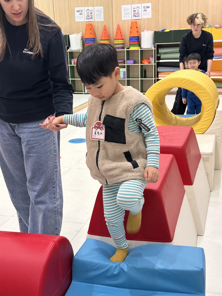폼 블록 계단을 오르는 아이와 옆에서 손을 받쳐 주는 선생님